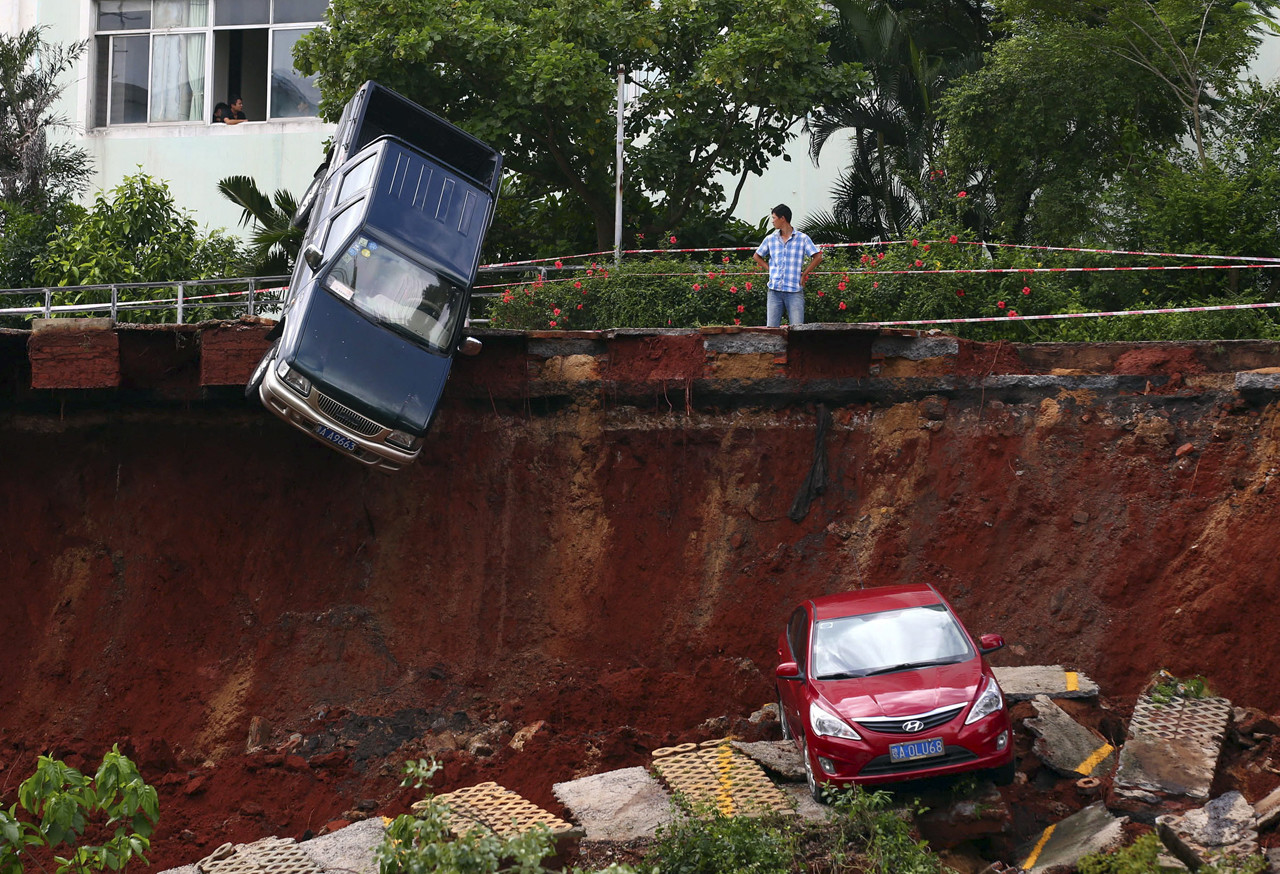 A giant sinkhole has swallowed up a parking lot in Haikou China, parking collapse haikou china landslide, landslide haikou china, sinkhole swallows parking lot china haikou, A man looks on as cars are seen stuck in a sinkhole that occurred in a parking area after heavy rainfall hit Haikou, A giant sinkhole has swallowed up a parking lot in Haikou, China. Photo: Reuter