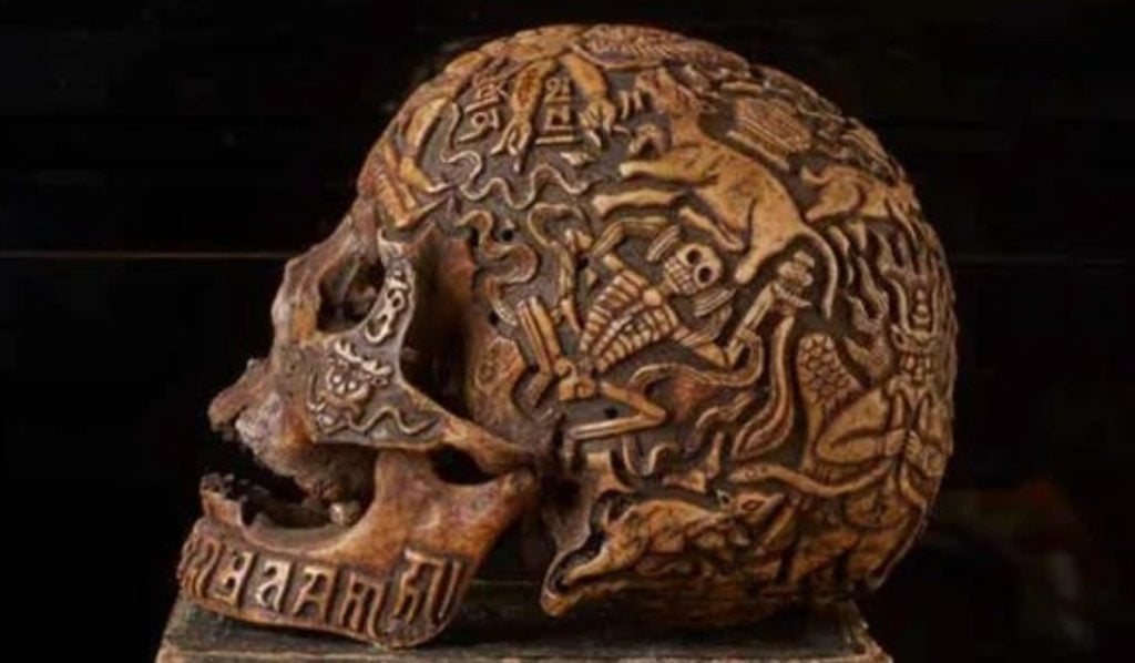 Carved Tibetan Yama skull with intricate bone engravings depicting skeletons, animals, and symbols.