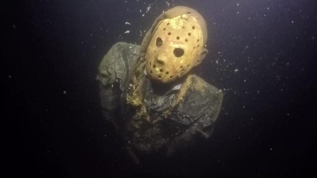 Life-size Jason Voorhees statue submerged underwater in Cayuga Mine Pit, Minnesota, appearing ghostly in the dark lake depths.