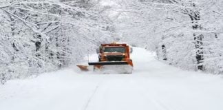 5 Rare Weather Phenomena That Cause Loud Booming Noises Orange snowplow clearing a snowy forest road during a heavy winter storm, symbolizing rare weather phenomena that cause loud booming sounds like thundersnow and ice quakes