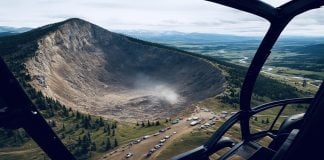 Wyoming Mountain Collapses Into Itself, Leaving Giant Crater West of Casper Helicopter cockpit framing a huge collapsed mountain crater west of Casper, Wyoming, with emergency vehicles and crews gathered along the rim.