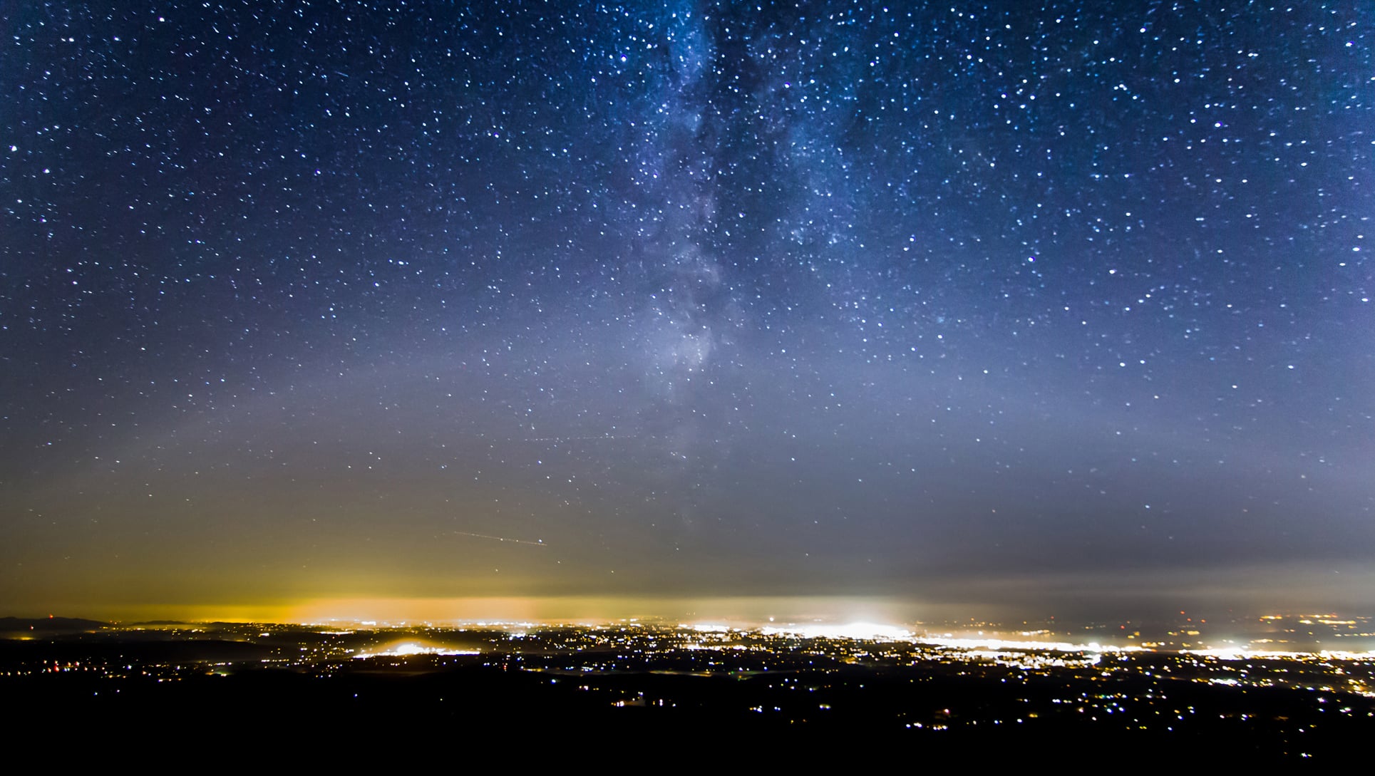 City lights glow on the horizon, brightening the night sky and washing out stars.