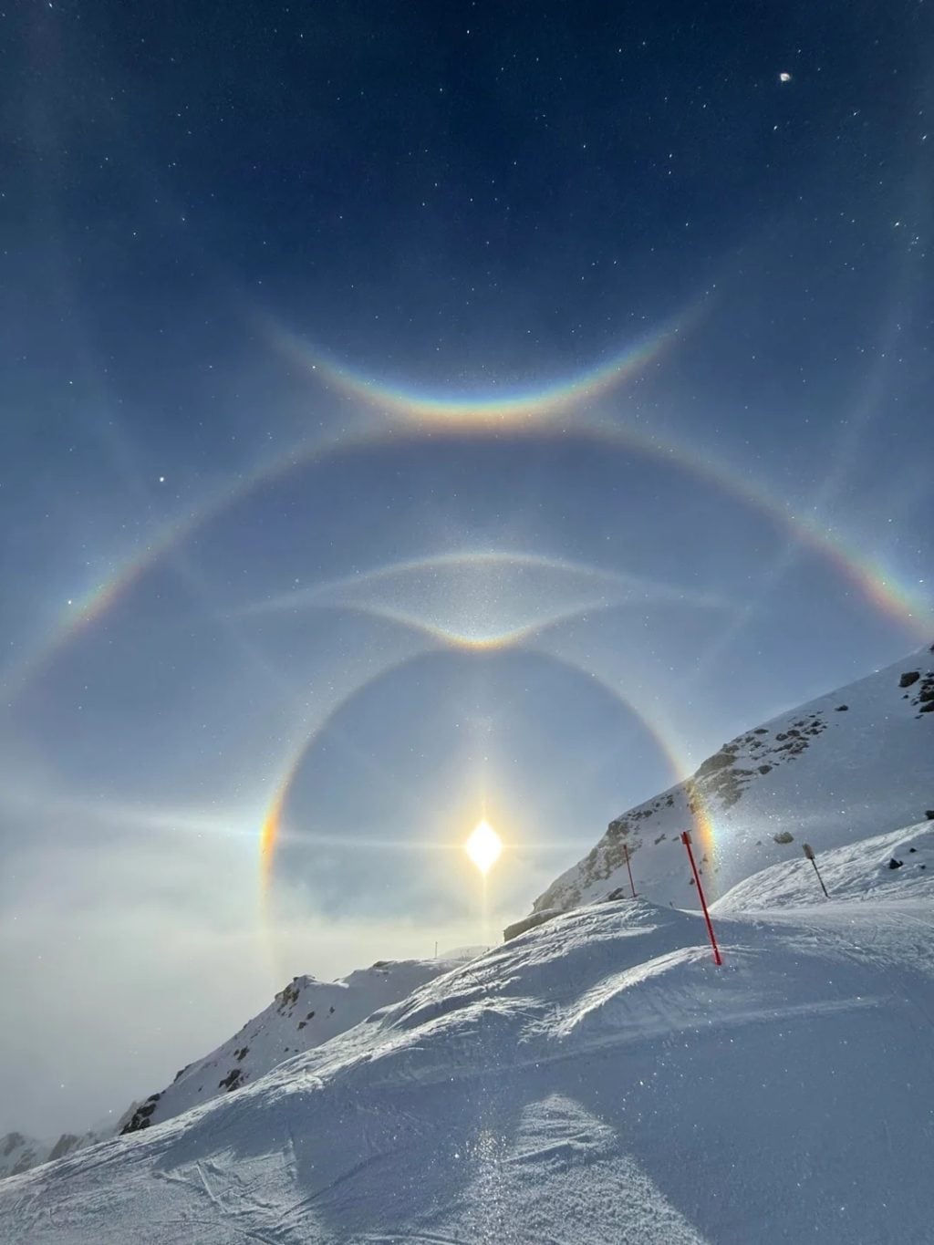 Multiple solar halos and light arcs surrounding the sun over snowy mountains in Arosa, Switzerland