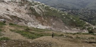 DR Congo Coltan Mine Landslide Kills 200+: How Heavy Rainfall Triggers Sudden Slope Failure (Mar 2026) Wide view of a massive landslide scar on a hillside after heavy rainfall, with a person standing in the foreground for scale